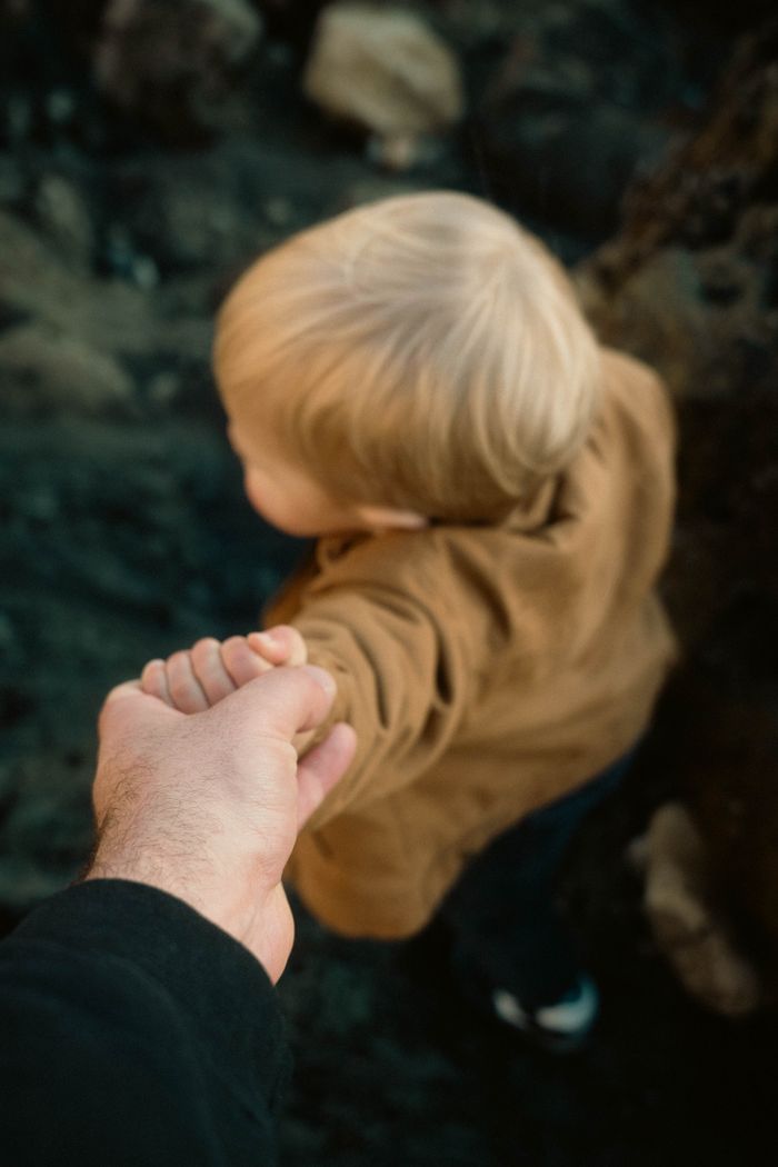 A parent holding a child's hand as they explore an outdoor setting together.