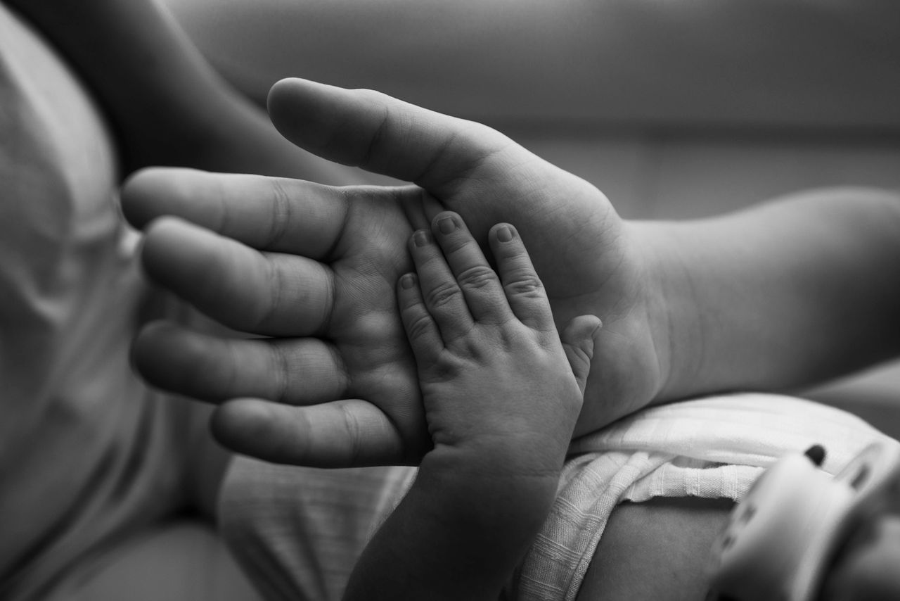 Close-up black and white photo of baby hand gently held by adult's palm, symbolizing love and connection.